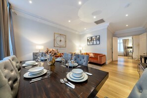 Ein Essbereich mit einem dunklen Holztisch, gedeckt für sechs Personen, der von zwei Sofas flankiert wird, eines mit einer gesteppten Rückenlehne und das andere mit einem weichen, orangefarbenen Stoff.