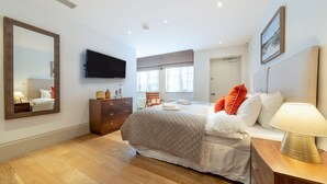 A bedroom with a bed, a dresser, a TV, and a window. - Royal 4 Bedroom Apartment (London)