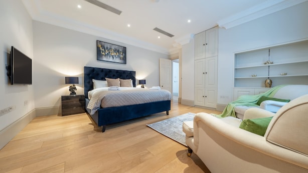 A modern bedroom with a bed, a TV, a sofa, and a wardrobe. - Royal 4 Bedroom Apartment (London)