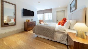 A hotel room with a large bed, a dresser, a TV mounted on the wall, and a window with curtains. - Royal 4 Bedroom Apartment (London)