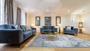 A modern living room with a blue sofa set, a coffee table, and decorative mirrors. - Exquisite 3-bedroom House in Mayfair (London)