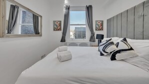 Ein Hotelzimmer mit einem großen Bett, einem Fenster mit Vorhängen, einem Spiegel und Bildern an den Wänden.