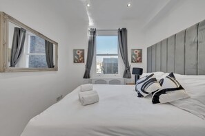 Ein Hotelzimmer mit einem großen Bett, einem Fenster mit Vorhängen, einem Spiegel und Bildern an den Wänden.