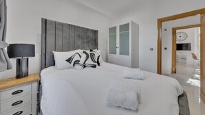 Ein modernes Hotelzimmer mit einem großen Bett, einem Nachttisch mit Lampe, einem Kleiderschrank und Blick auf den Speiseraum.