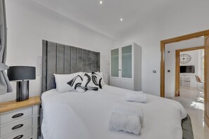 Ein modernes Hotelzimmer mit einem großen Bett, einem Nachttisch mit Lampe, einem Kleiderschrank und Blick auf den Speiseraum.