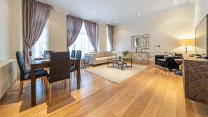 A modern living room with a dining area, a sofa, a coffee table, and a TV. - Superior 2 Bedroom Apartment in Mayfair (London)