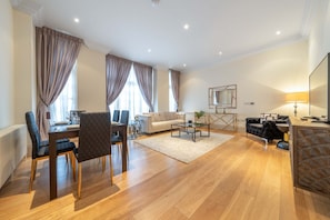 A modern living room with a dining area, a sofa, a coffee table, and a TV. - Superior 2 Bedroom Apartment in Mayfair (London)
