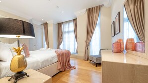 A modern hotel room with a bed, bedside lamp, and a desk with a lamp. - Superior 2 Bedroom Apartment in Mayfair (London)