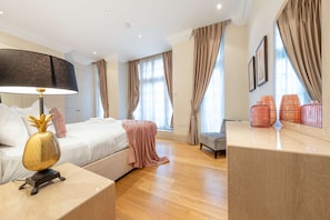 A modern hotel room with a bed, bedside lamp, and a desk with a lamp. - Superior 2 Bedroom Apartment in Mayfair (London)