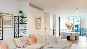 A modern living room with a sectional sofa, a decorative shelf with artwork, and a view to the outside. - Luxury 4-bed Duplex Penthouse in Battersea (London)