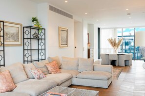 Ein modernes Wohnzimmer mit einem Ecksofa, einem Deko-Regal mit Kunstwerken und Blick ins Freie.