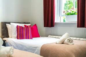 Ein ordentlich bezogenes Bett mit weißen und rosafarbenen Kissen, einer beigen Decke und einem aufgerollten Handtuch auf einer weißen Matratze.