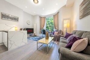 Ein modernes Wohnzimmer mit einer Couch, einem Couchtisch, einem Fernseher und einer Küchenzeile mit Kühlschrank.