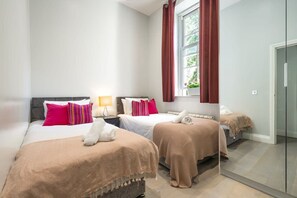 Ein Hotelzimmer mit zwei Betten, einem Fenster mit Vorhängen, einem Nachttisch mit Lampe und einer Tür.