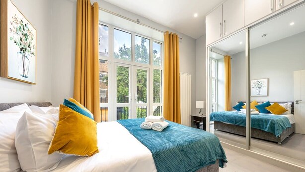 A hotel room with two beds, large windows, a mirror, and artwork on the walls. - Exclusive 3-bedroom Apartment (London)