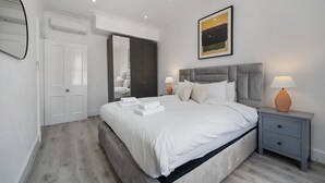 A modern bedroom with a large bed, bedside tables, a wardrobe, and a painting on the wall. - Standard 1 Bedroom Apartment In Belgravia (London)