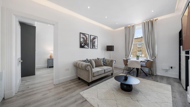 A modern living room with a sofa, a dining table, and a rug. - Standard 1 Bedroom Apartment In Belgravia (London)