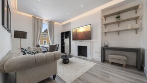 A modern living room with a sofa, a fireplace, and a TV mounted on the wall. - Standard 1 Bedroom Apartment In Belgravia (London)