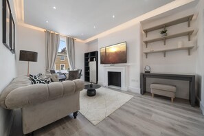 A modern living room with a sofa, a fireplace, and a TV mounted on the wall. - Standard 1 Bedroom Apartment In Belgravia (London)