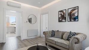 A modern living room with a beige sofa, a round coffee table, and two abstract paintings on the wall. - Standard 1 Bedroom Apartment In Belgravia (London)