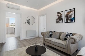 A modern living room with a beige sofa, a round coffee table, and two abstract paintings on the wall. - Standard 1 Bedroom Apartment In Belgravia (London)