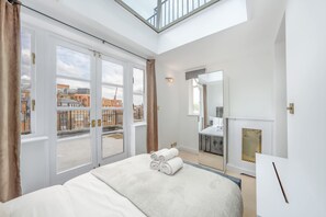 A modern hotel room with a large bed, a skylight, a view of the city, and a fireplace. - Modern 4-bed Apartment in Knightsbridge (London)