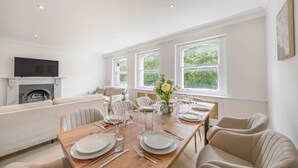 Ein Essbereich mit einem Holztisch, gedeckt für sechs Personen, einem Kamin und einer Couch im Hintergrund.