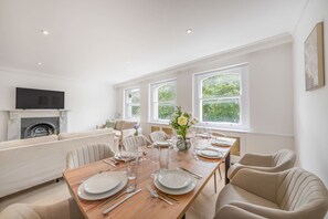 A dining area with a wooden table set for six, a fireplace, and a sofa in the background. - Modern 4-bed Apartment in Knightsbridge (London)