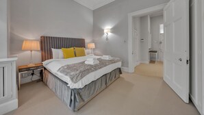 Una camera da letto con un letto, lampade sui comodini, un tavolino notte e una porta che dà su un'altra stanza.