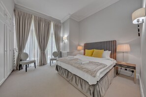 Ein Hotelzimmer mit einem großen Bett, zwei Nachttischen, einem Sessel, einem Schreibtisch und einer Lampe.