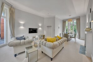 Ein modernes Wohnzimmer mit einer Couch, einem Couchtisch und einem Fernseher. Es gibt eine Essecke mit Tisch und Stühlen.