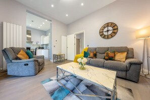Ein Wohnzimmer mit Sofa, Sessel, Couchtisch und einer Wanduhr.