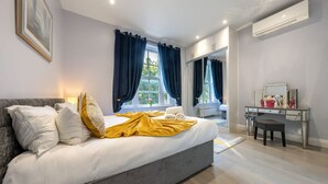 A bedroom with a bed, a desk, and a window with curtains. - Deluxe 2 Bedroom Apartment (London)