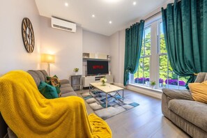 Ein modernes Wohnzimmer mit einer Couch, einem Couchtisch, einem Fernseher und einem Fenster mit Vorhängen.