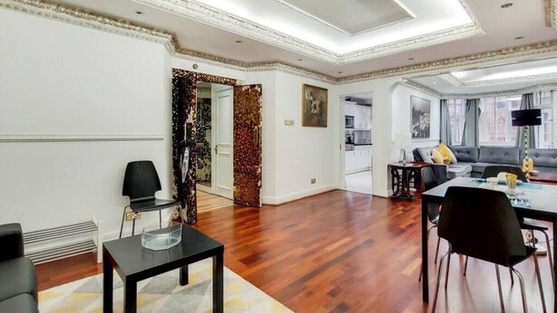 A spacious living area with a dining table, chairs, a sofa, and a TV. - Superior Three Bedroom Apartment Opposite Harrods (London)