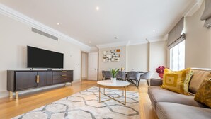 A modern living room with a flat-screen TV, a sofa, a dining table, and a patterned rug. - Super Deluxe 2 Bedroom Apartment in Mayfair (London)