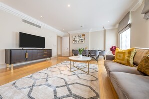 Ein modernes Wohnzimmer mit Flachbildfernseher, einer Couch, einem Esstisch und einem gemusterten Teppich.
