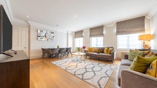 A modern living room with a sofa, dining table, and chairs, a coffee table, and a TV. - Super Deluxe 2 Bedroom Apartment in Mayfair (London)