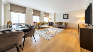 A modern living room with a dining area, wooden flooring, and a flat-screen TV. - Super Deluxe 2 Bedroom Apartment in Mayfair (London)