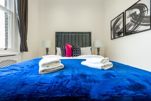 Ein Hotelzimmer mit einem großen Bett, zwei Nachttischlampen, einem Kopfteil und Kunstwerken an der Wand.