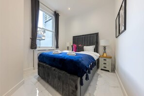 Ein Schlafzimmer mit Bett, Fenster, Nachttisch und Lampe.