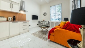 A modern kitchen with white cabinets, a stainless steel range hood, and a dining area with a table and chairs.