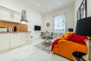 A modern kitchen with white cabinets, a stainless steel range hood, and a dining area with a table and chairs.