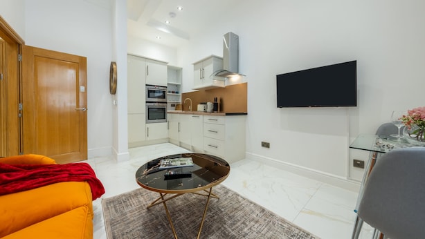 A compact living space with a kitchenette, a dining area, and a TV mounted on the wall.