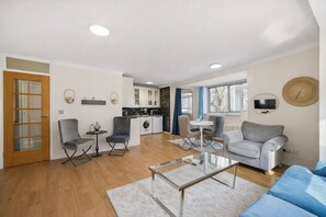 Ein modernes Wohnzimmer mit Glastisch, grauen Sofas und einer Küche im Hintergrund.