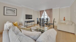 Ein modernes Wohnzimmer mit einer Couch, einem Glastisch, einem Fernseher und einem Essbereich mit Stühlen und einem Tisch.