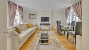 Ein modernes Wohnzimmer mit Sofa, Couchtisch, Fernseher und einem Essbereich mit Stühlen und Tisch.