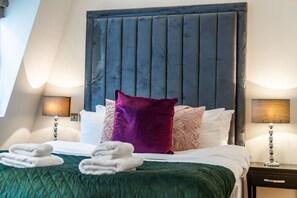 Ein Hotelzimmer mit Bett, Kissen, Kopfteil, Nachttisch und einer Lampe.