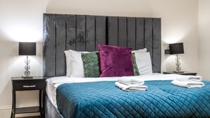 A neatly made bed with a blue quilt, two pillows, and a headboard. - Royal Two Bedroom House in Mayfair (London)