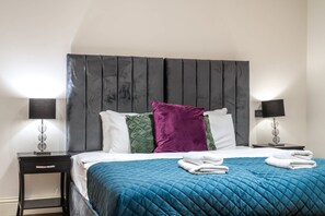 Ein ordentlich bezogenes Bett mit einer blauen Stegdecke, zwei Kissen und einem Kopfteil.